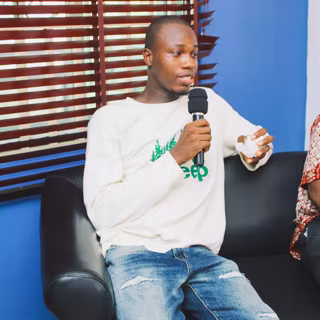 Yves on a sofa speaking into a microphone on a panel
