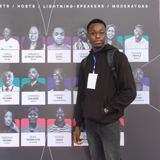Yves in front of the speakers board at an event, with his own name on it